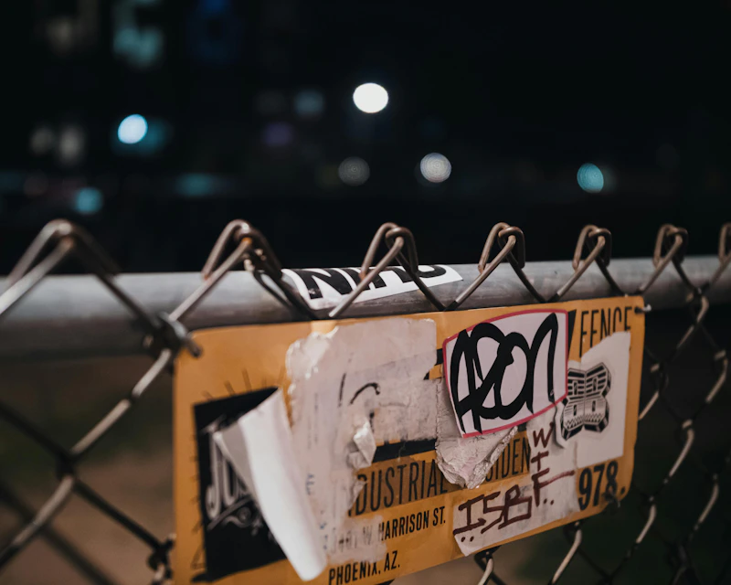 Graffiti stickers on a chain-link fence at night.